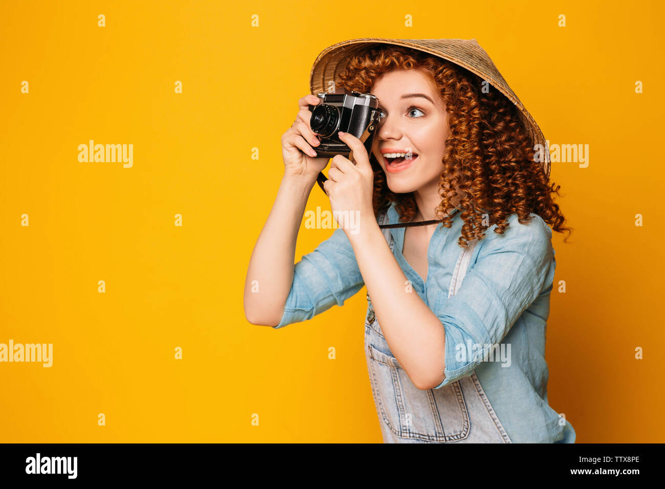 Lächelnd curly rothaarige Frau mit chinesischen Hut holding Foto Kamera und Foto auf gelben Hintergrund. Tourismus und Reisen Stockfoto