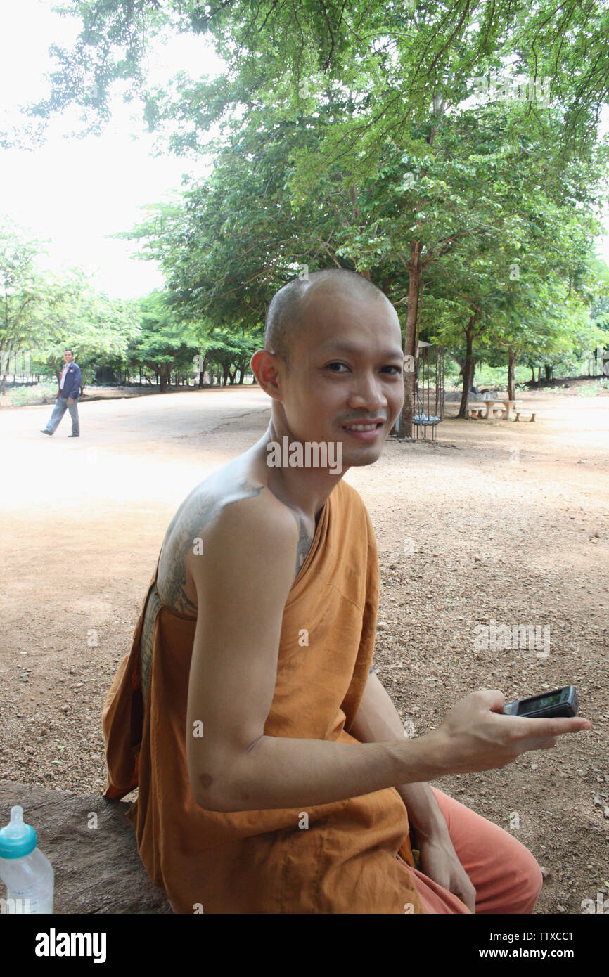 Mönch, der auf einem Felsbrocken sitzt und Textnachrichten aussahen, Tiger Temple, Sai Yok, Kanchanaburi, Thailand Stockfoto