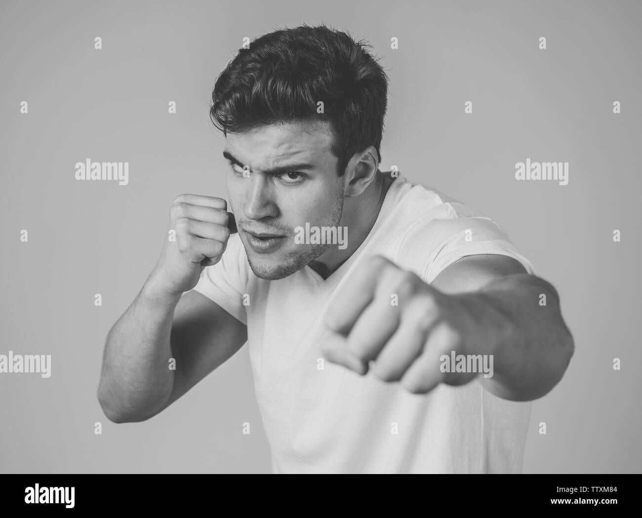 Junger attraktiver Mann in Rage suchen wütend in der Verteidigung Haltung und drohen Stanzen mit Faust in der wütenden umgekippt und wütenden Gesichtsausdruck isoliert Grau ba Stockfoto