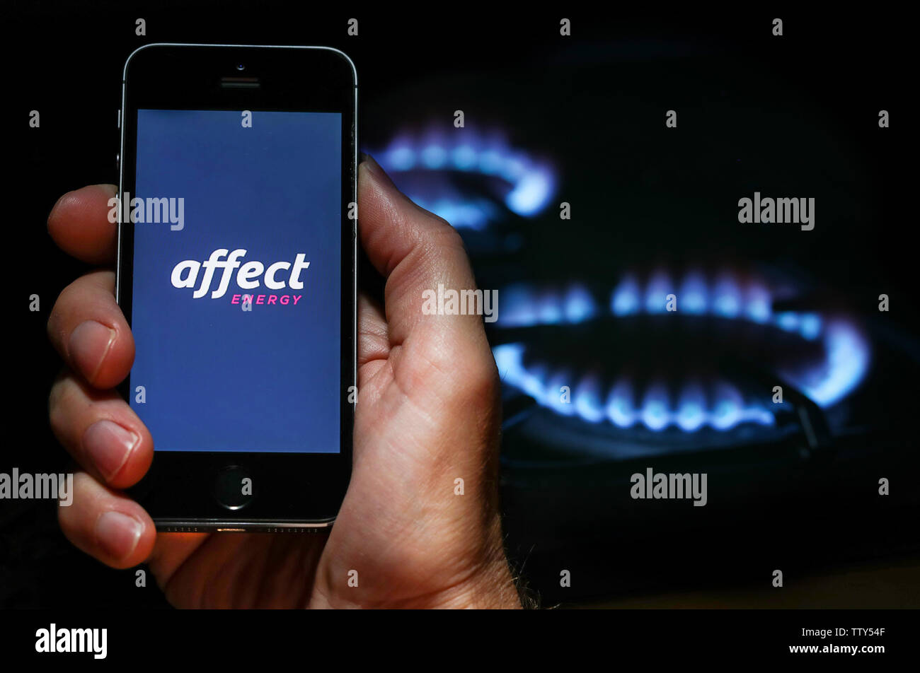 Ein Mann auf der Website Logo auf der Suche nach Energie unternehmen Energie Einfluss auf sein Handy vor seinem Gaskocher (Editorial nur verwenden) Stockfoto