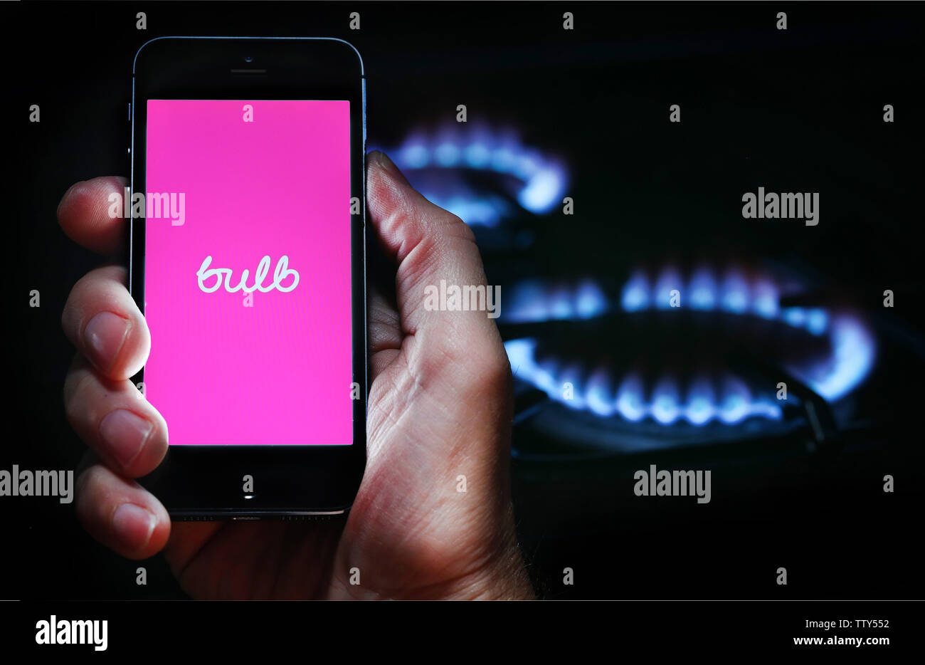 Ein Mann auf der Website Logo auf der Suche nach Energie Firma Lampe auf seinem Mobiltelefon vor seinem Gaskocher (Editorial nur verwenden) Stockfoto