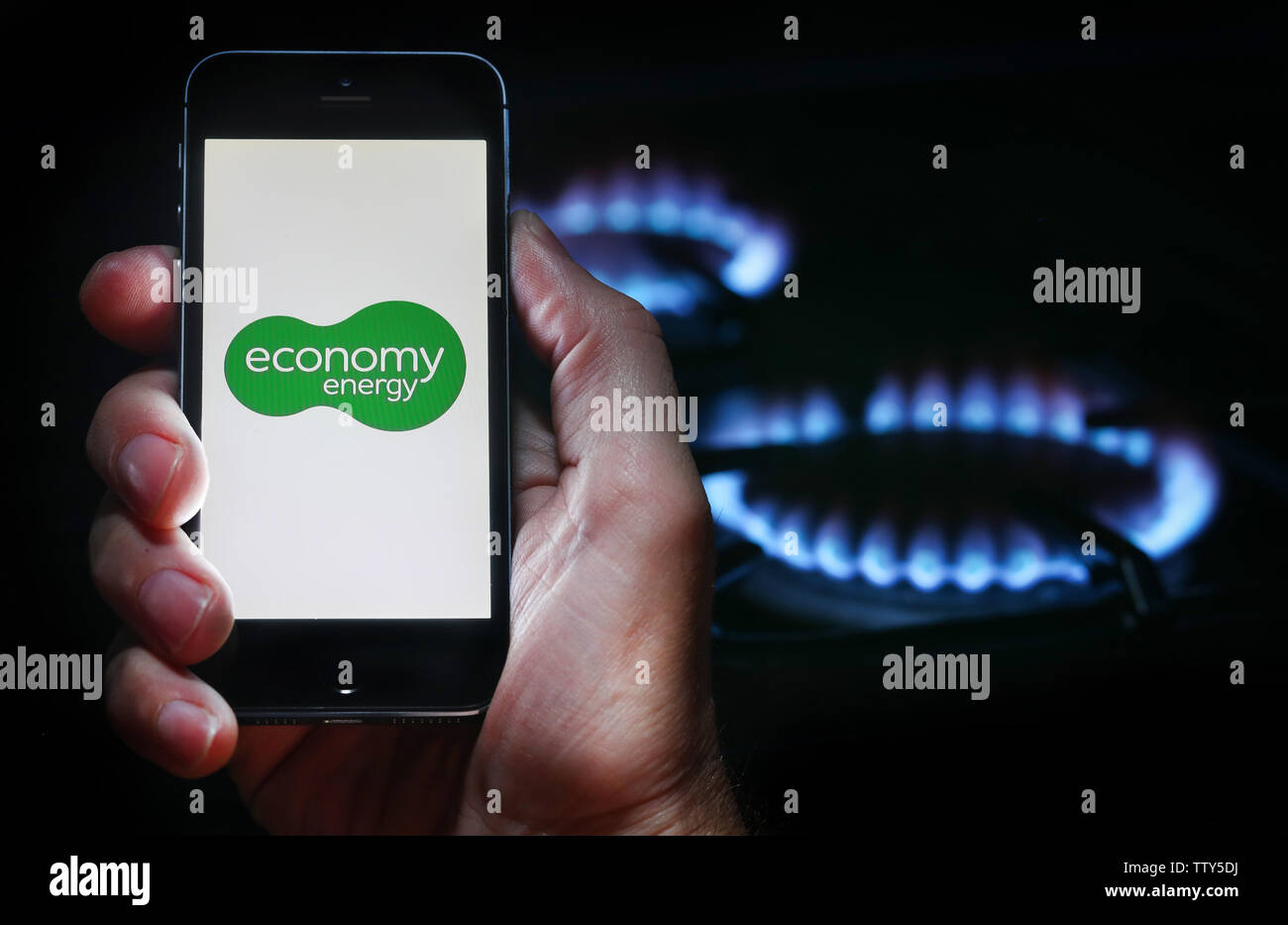Ein Mann auf der Website Logo auf der Suche nach Energie unternehmen Wirtschaft Energie auf seinem Mobiltelefon vor seinem Gaskocher (Editorial nur verwenden) Stockfoto