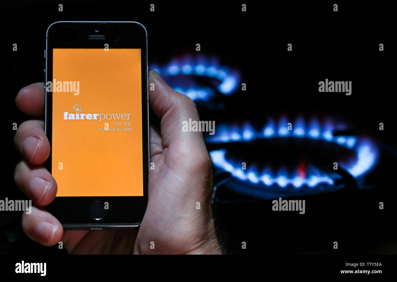 Ein Mann auf der Website Logo für Energieunternehmen gerechtere Macht auf sein Handy vor seinem Gaskocher (Editorial nur verwenden) Stockfoto