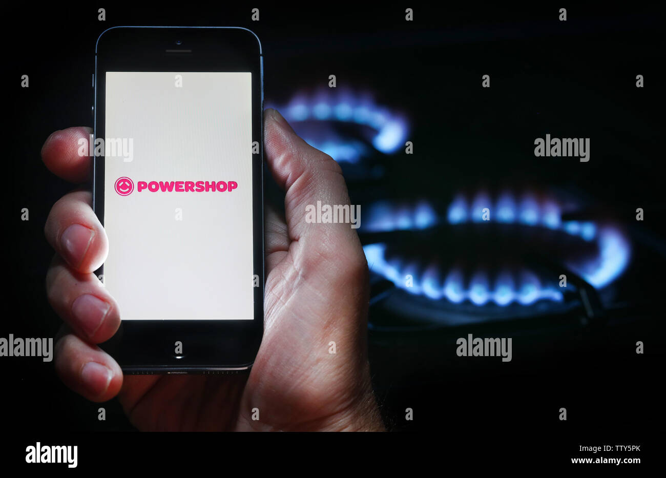 Ein Mann auf der Website Logo auf der Suche nach Energie unternehmen Powershop auf seinem Mobiltelefon vor seinem Gaskocher (Editorial nur verwenden) Stockfoto