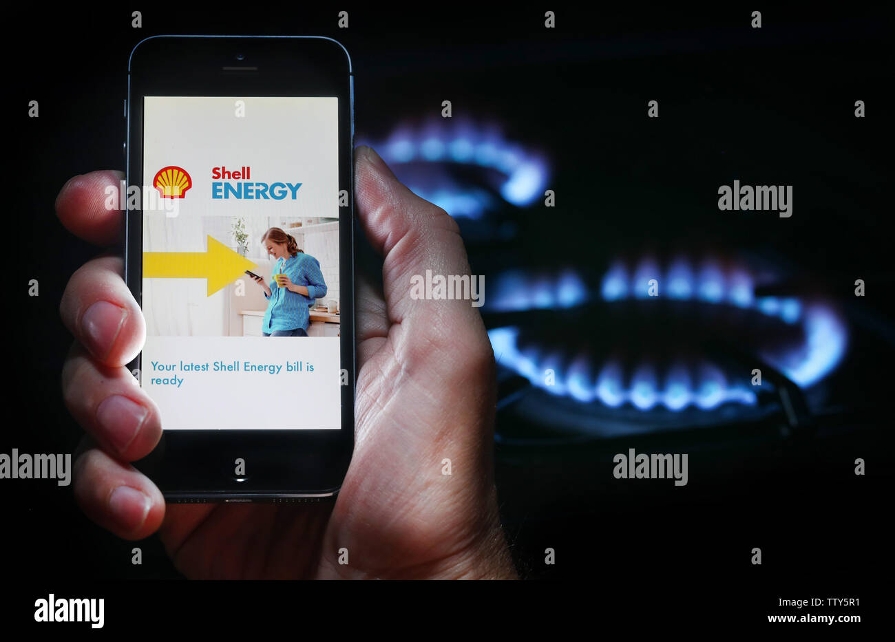Ein Mann, der an seine Rechnung von Energieunternehmen Shell Energy auf seinem Mobiltelefon vor seinem Gasherd suchen (Redaktionelle nur verwenden) Stockfoto