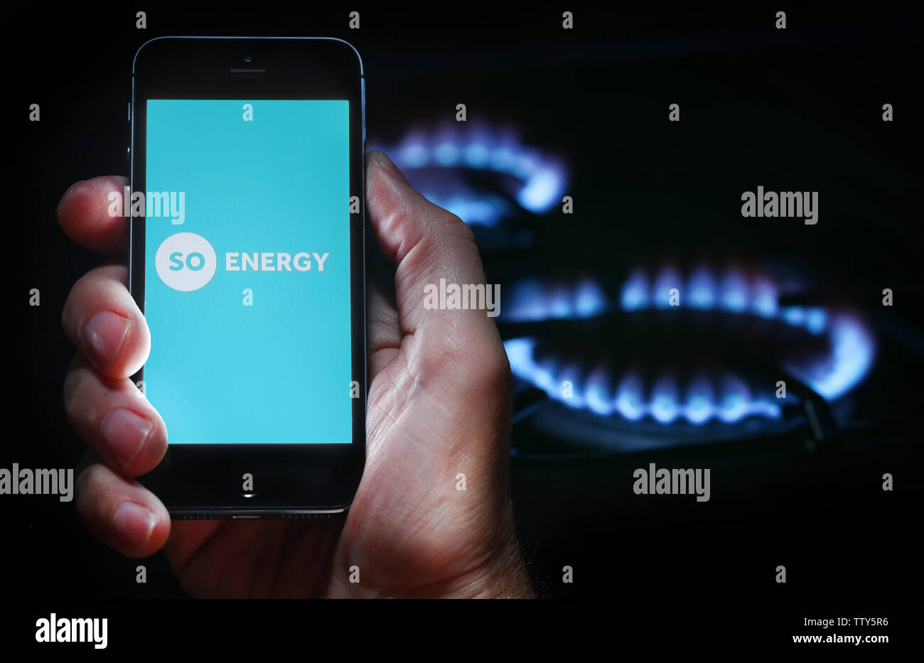 Ein Mann auf der Website Logo auf der Suche nach Energie unternehmen Energie auf seinem Mobiltelefon vor seinem Gaskocher (Editorial nur verwenden) Stockfoto