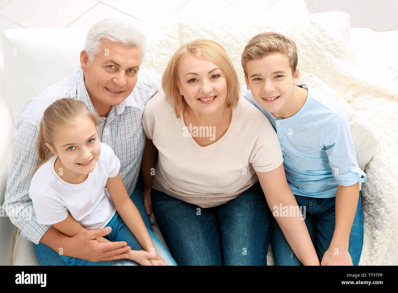 Niedliche Kinder mit Großeltern sitzen auf einem Sofa im Wohnzimmer. Stockfoto