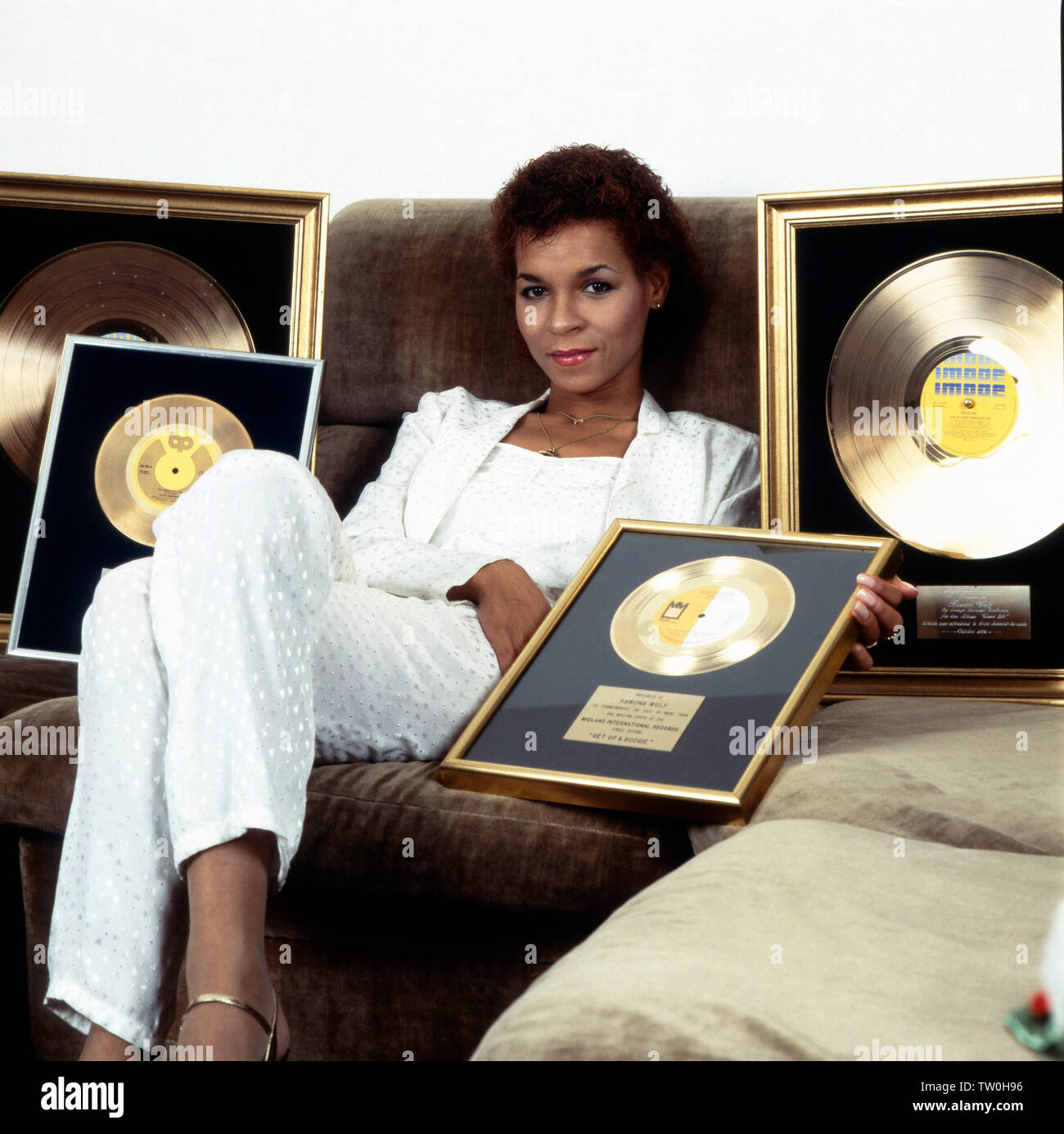 Homestory der deutschen Schlager - Disco- und Popsängerin Ramona Wulf 5/6 für sie auf dem Sofa ihre goldenen Schallplatten präsentiert, Deutschland Berlin ca. 1985. Homestory der Deutschen Pop, Disco und Pop Sängerin Ramona Wulf, während sie ihre Golden Records präsentiert auf dem Sofa, Deutschland Berlin ca. 1985. Stockfoto