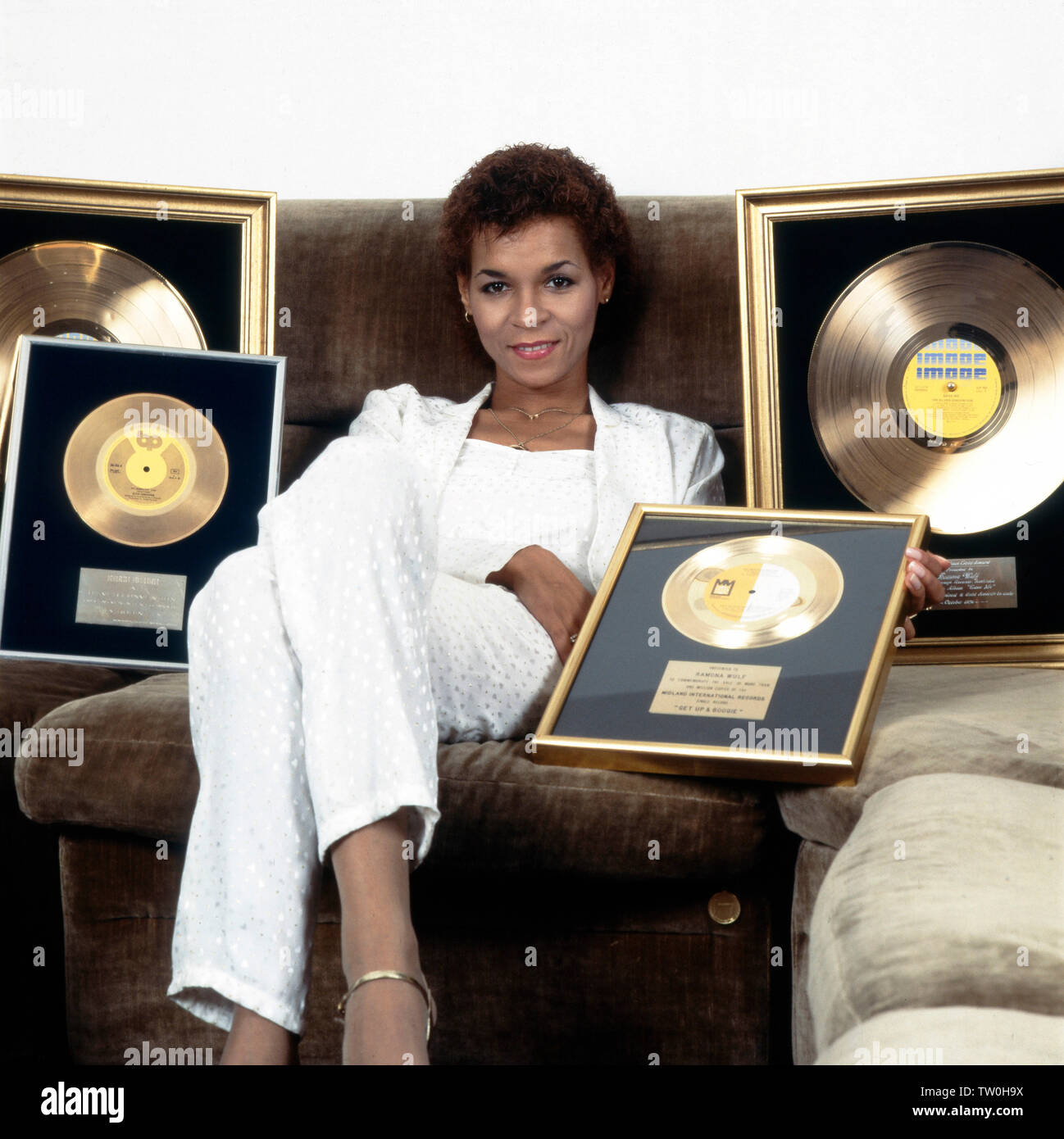 Homestory der deutschen Schlager - Disco- und Popsängerin Ramona Wulf 5/6 für sie auf dem Sofa ihre goldenen Schallplatten präsentiert, Deutschland Berlin ca. 1985. Homestory der Deutschen Pop, Disco und Pop Sängerin Ramona Wulf, während sie ihre Golden Records präsentiert auf dem Sofa, Deutschland Berlin ca. 1985. Stockfoto