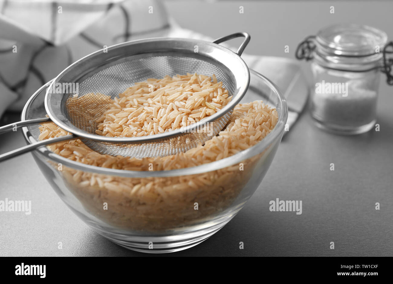 Sieb mit Raw brauner Reis in der Schüssel auf dem Tisch Stockfoto