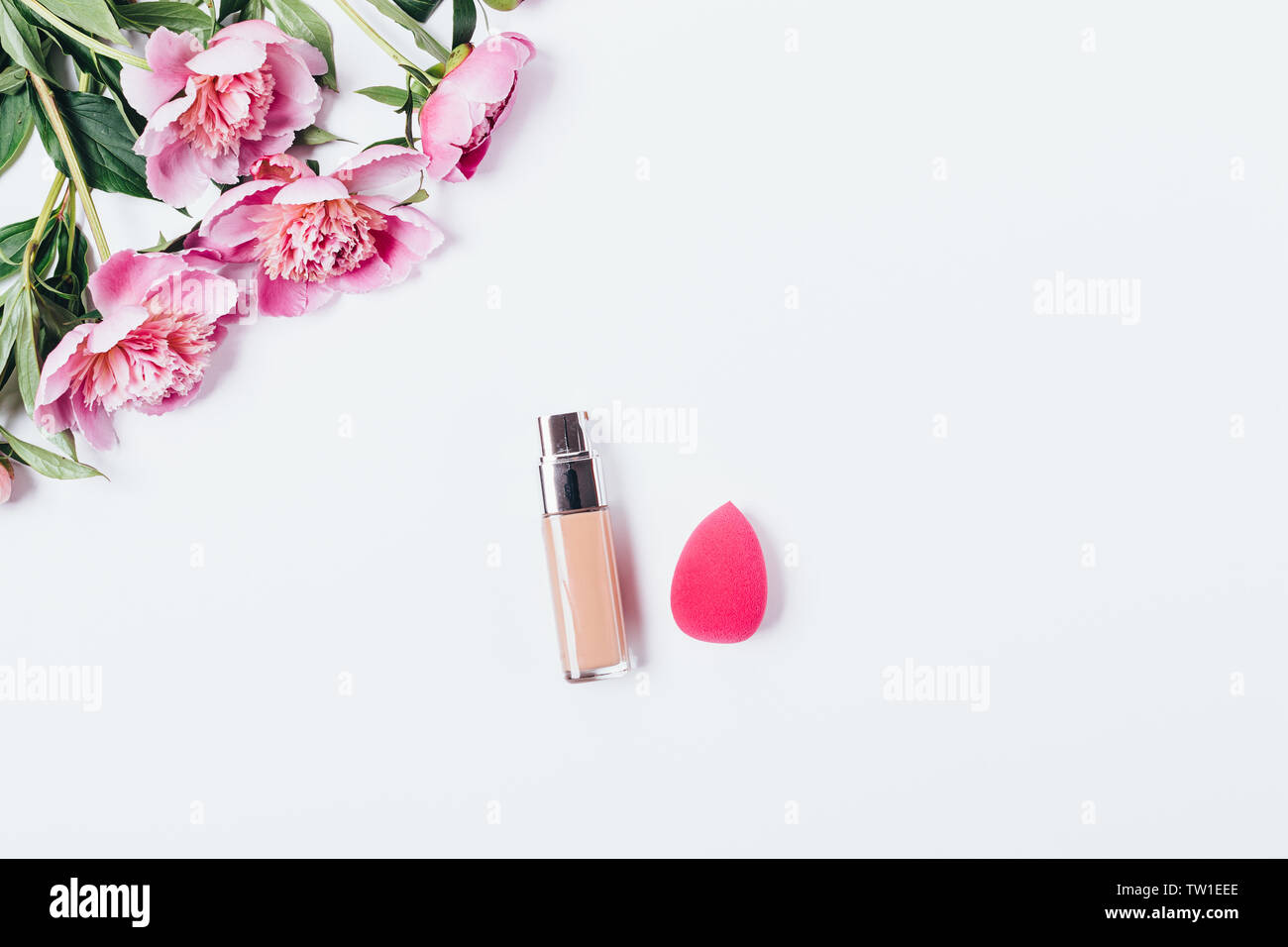 Make-up-blending schwamm Applikator und Gesichtsbehandlung Foundation Cream in der Nähe von Bouquet von rosa Pfingstrosen auf weißem Hintergrund, flach. Stockfoto