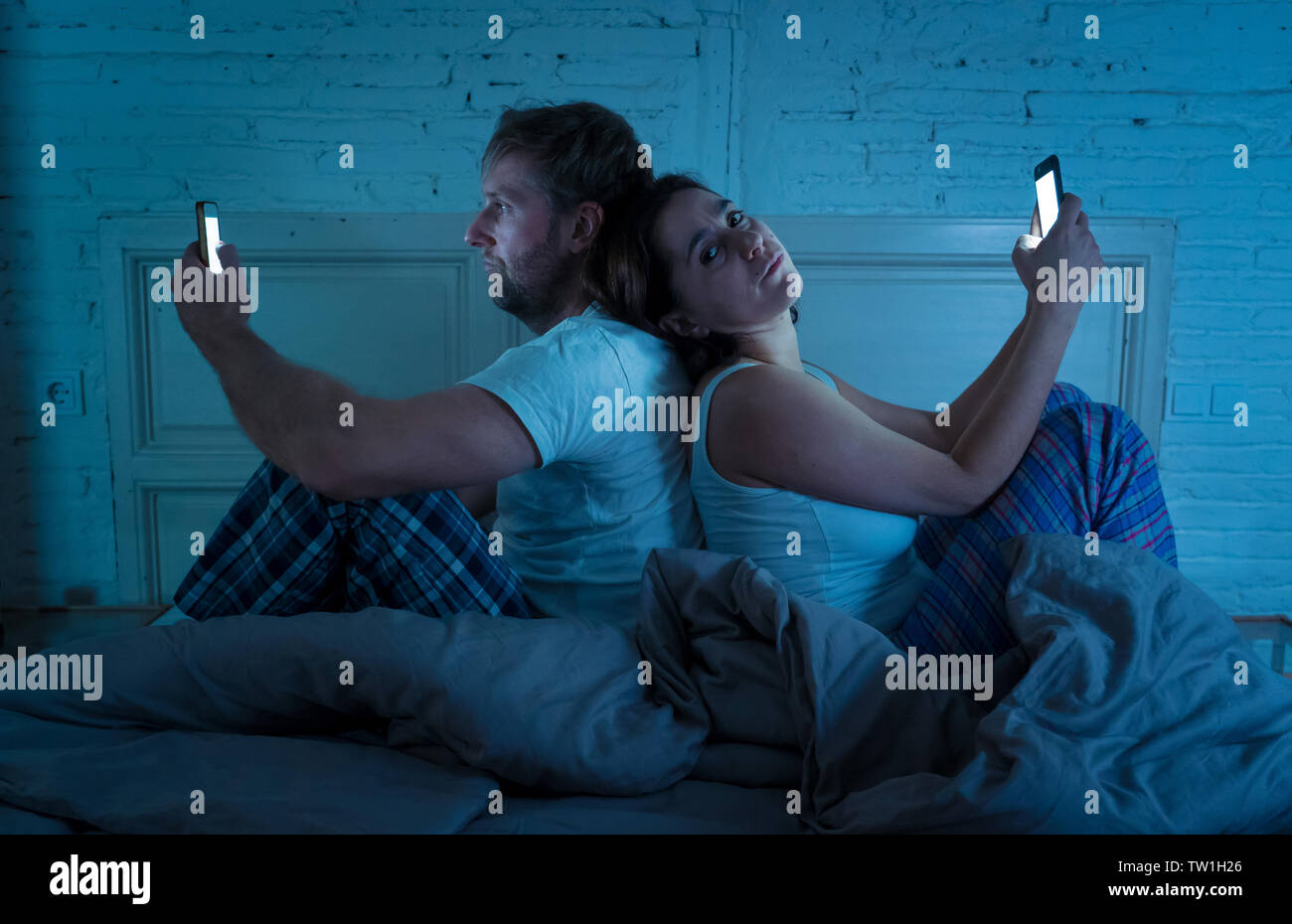 Traurige Mann und Frau Ehepaar mit Ihren smart Handy nachts im Bett gegenseitig ignorieren als Fremde in Beziehung und Kommunikation pro Stockfoto