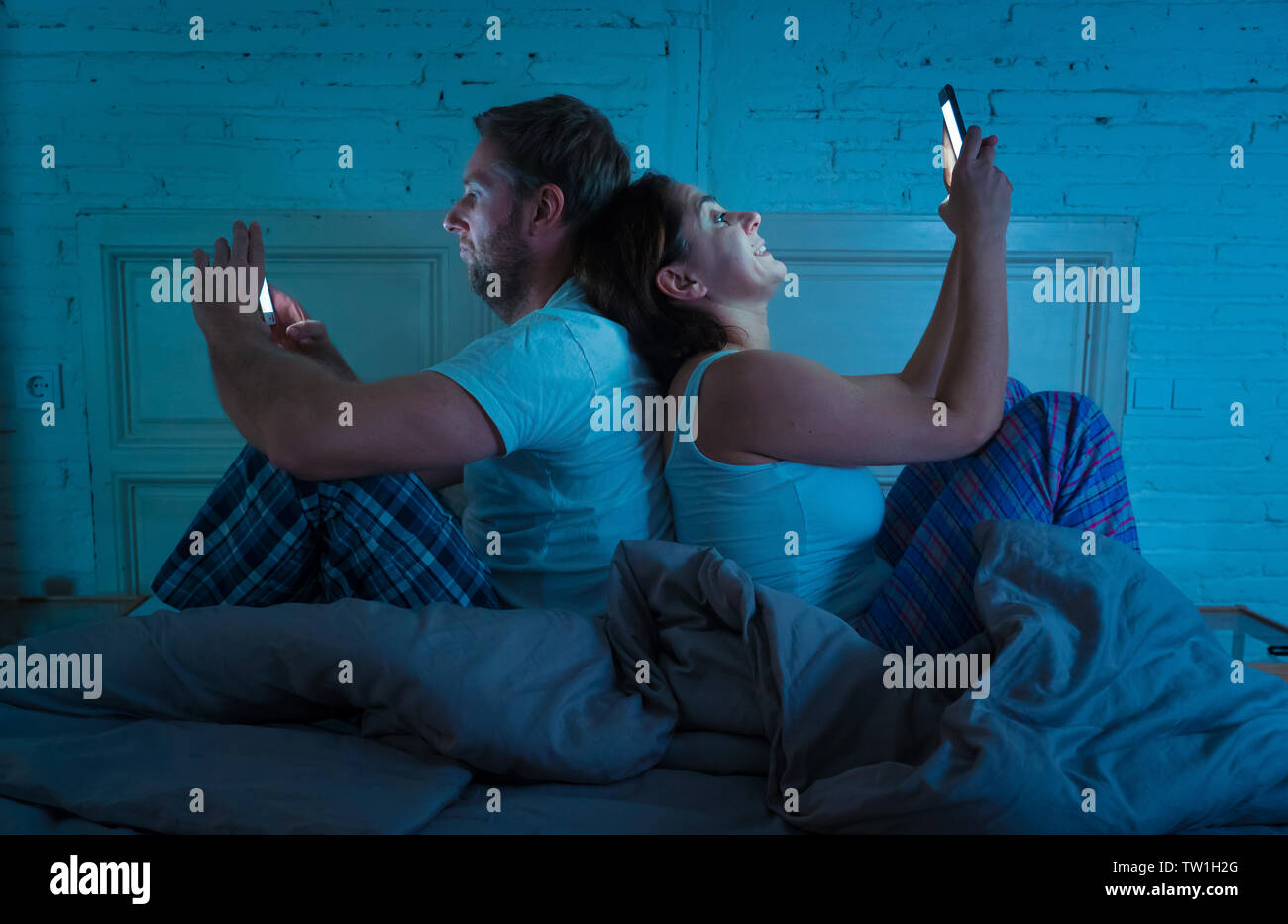 Paar im Bett mit Telefonen, Mann frustriert, enttäuscht und unzufrieden, während Internet-süchtiger Frau ihn ignoriert und genießt, Mobiltelefon, im sozialen Netz Stockfoto