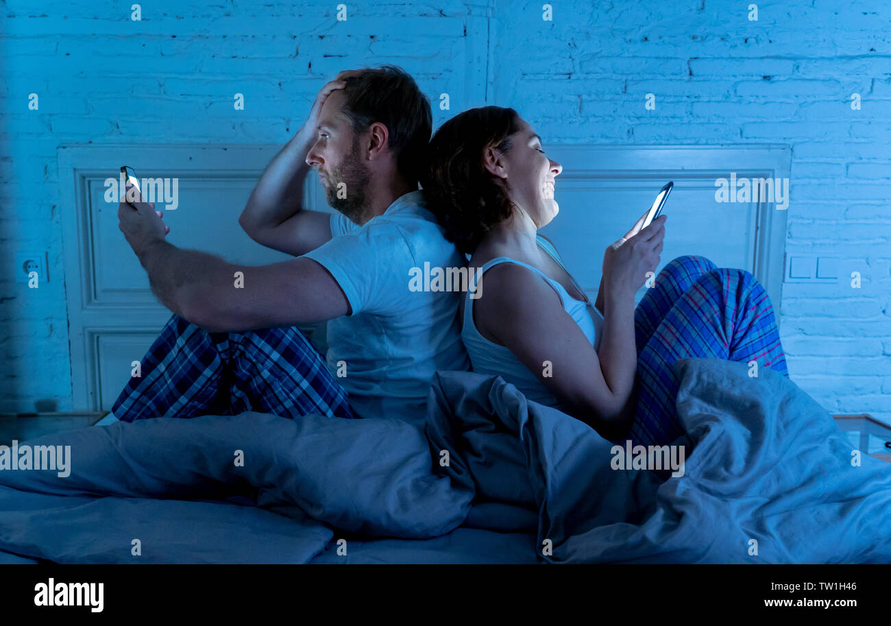 Paar im Bett mit Telefonen, Mann frustriert, enttäuscht und unzufrieden, während Internet-süchtiger Frau ihn ignoriert und genießt, Mobiltelefon, im sozialen Netz Stockfoto