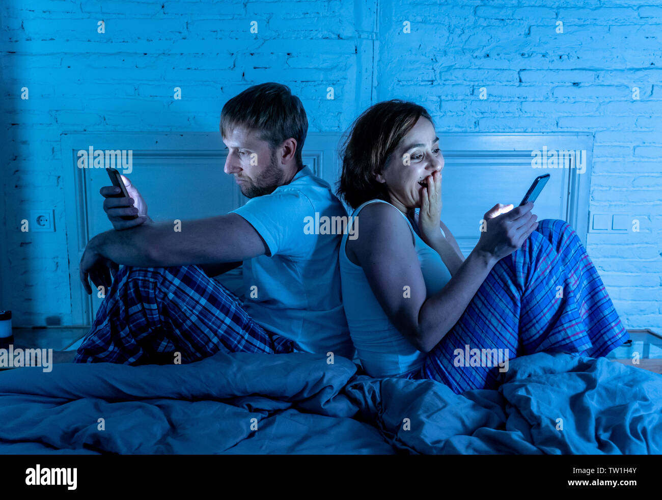 Paar im Bett mit Telefonen, Mann frustriert, enttäuscht und unzufrieden, während Internet-süchtiger Frau ihn ignoriert und genießt, Mobiltelefon, im sozialen Netz Stockfoto