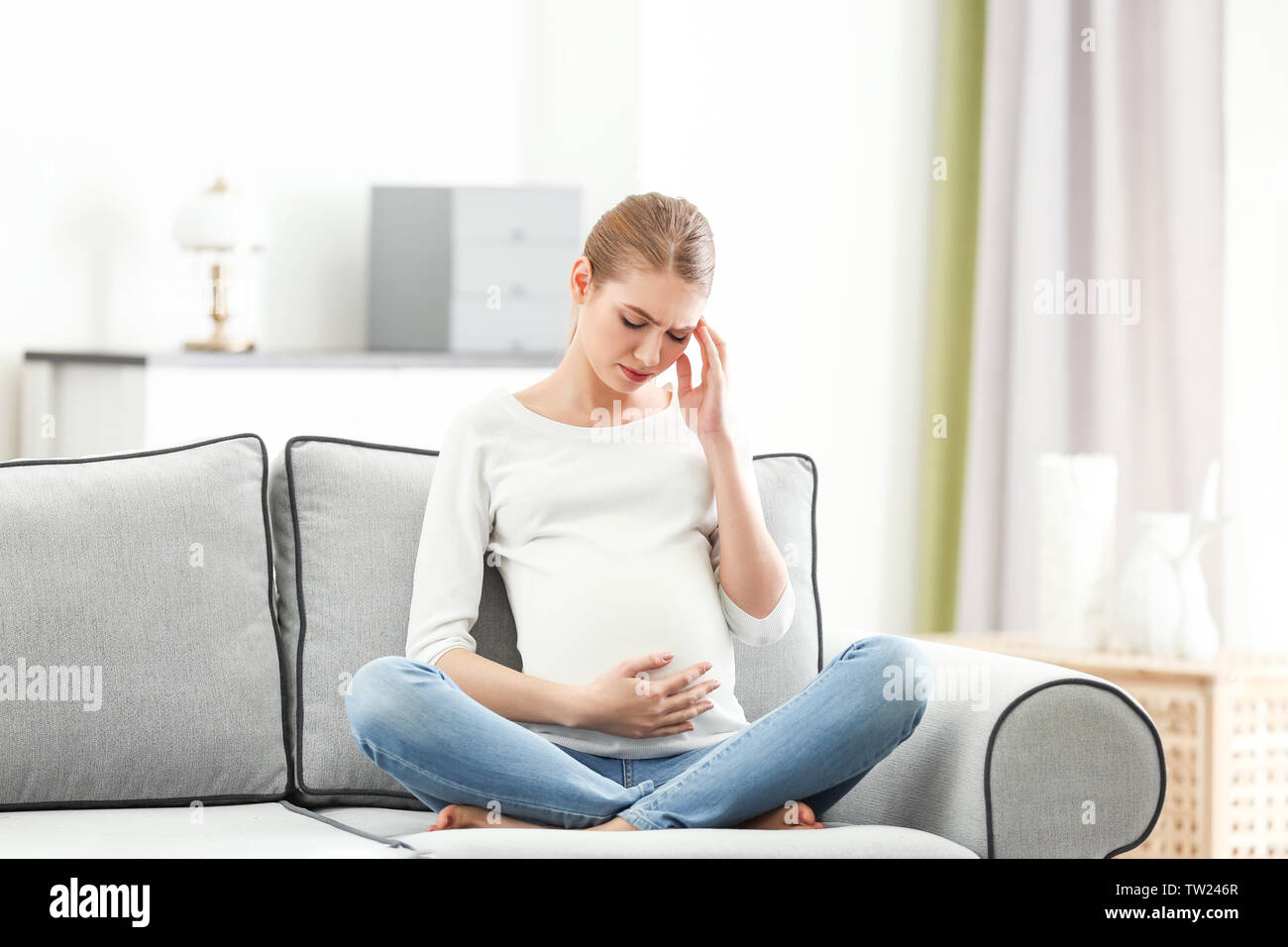 Schwangere Frau leidet unter Kopfschmerzen beim Sitzen auf dem Sofa zu Hause Stockfoto