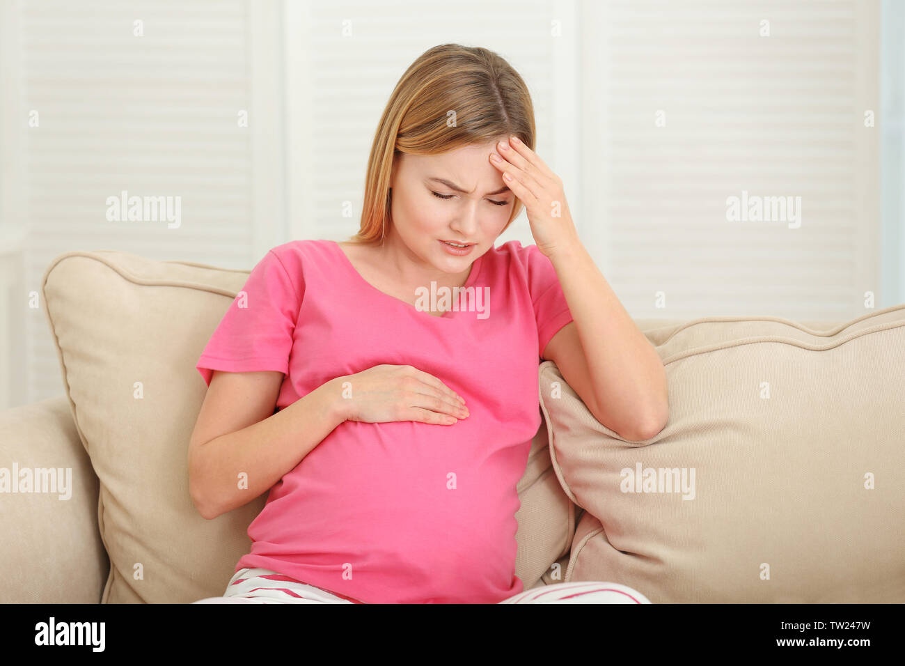 Schwangere Frau leidet unter Kopfschmerzen beim Sitzen auf dem Sofa zu Hause Stockfoto