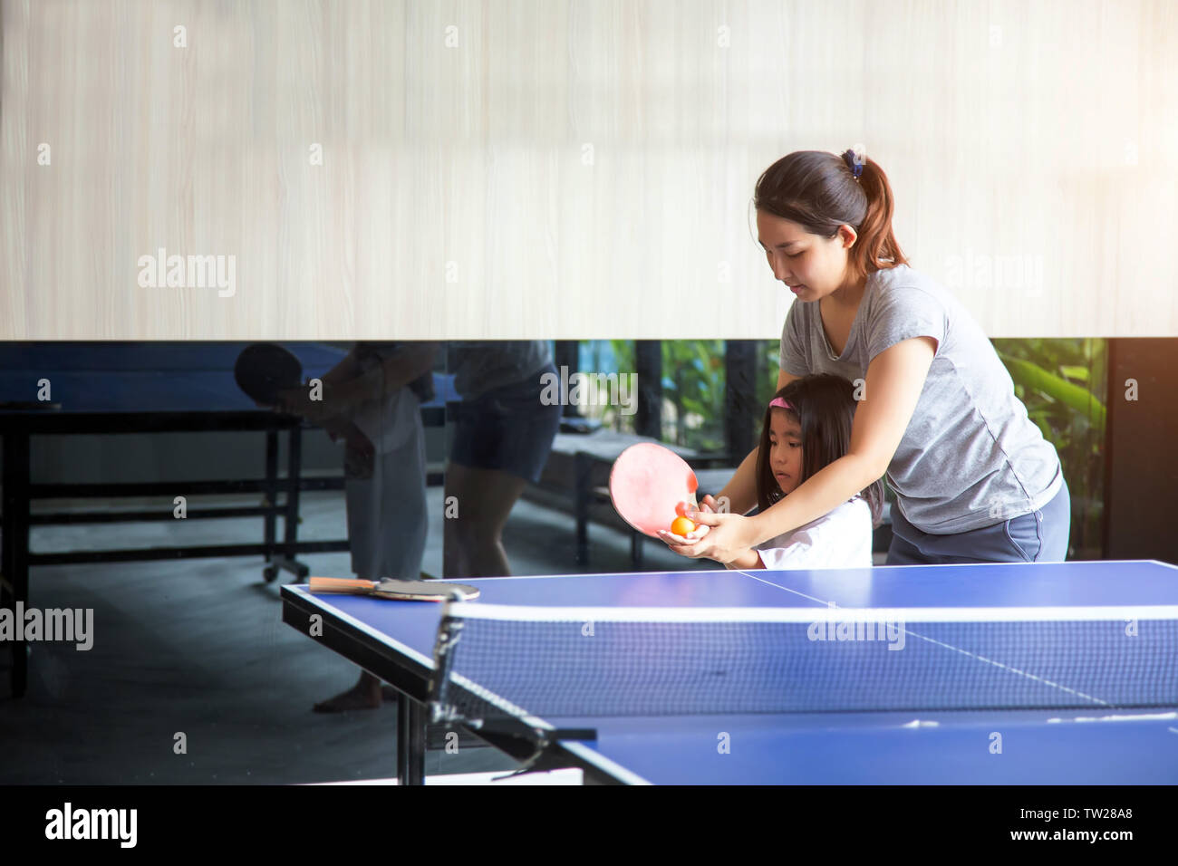 Asiatische Mutter und Kinder coaching Tischtennis spielen Sport Spiel auf Sommer Berufung. Mom halten Tochter Hand teble Tennis Schläger und Ball ist glücklich Mo Stockfoto