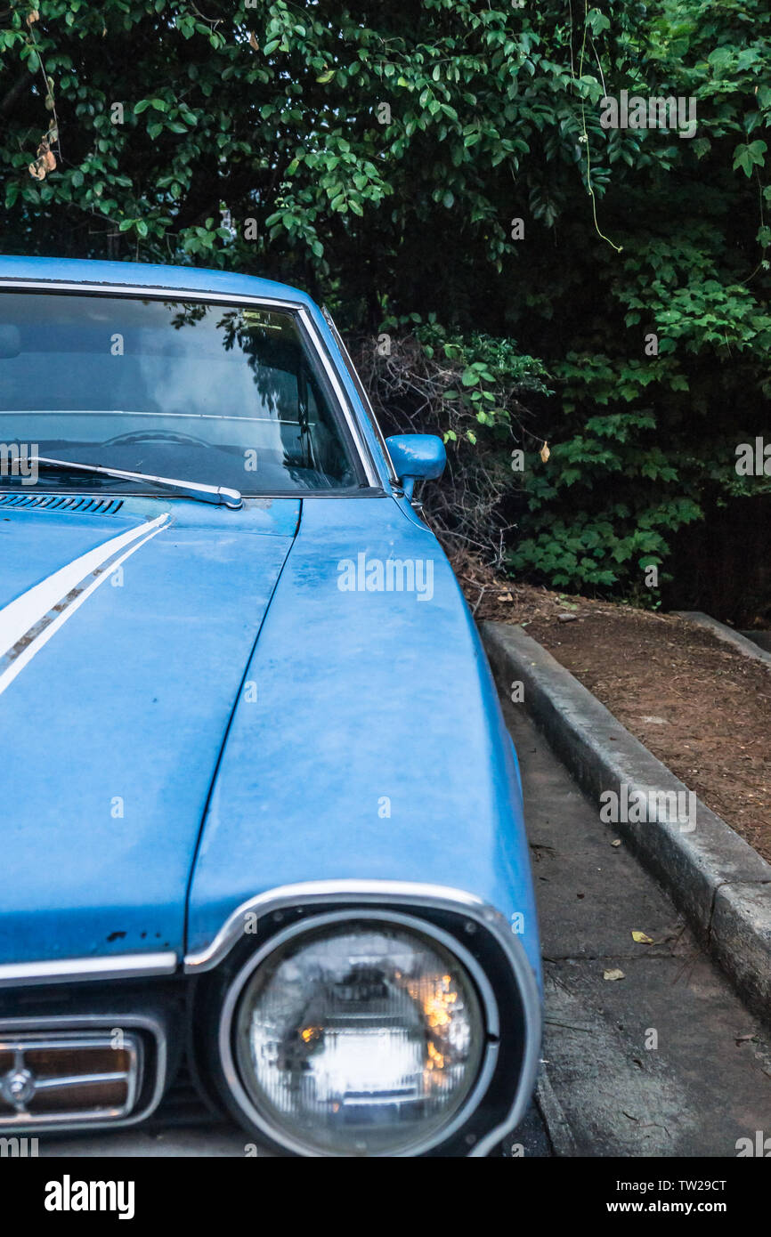 In der Nähe der alten Scheinwerfer's Vintage blaues Auto. Geparkt und umgeben von grünen Bäumen Laub außerhalb. Kein Mensch, aber in der Nähe der Fahrerseite hinten Stockfoto