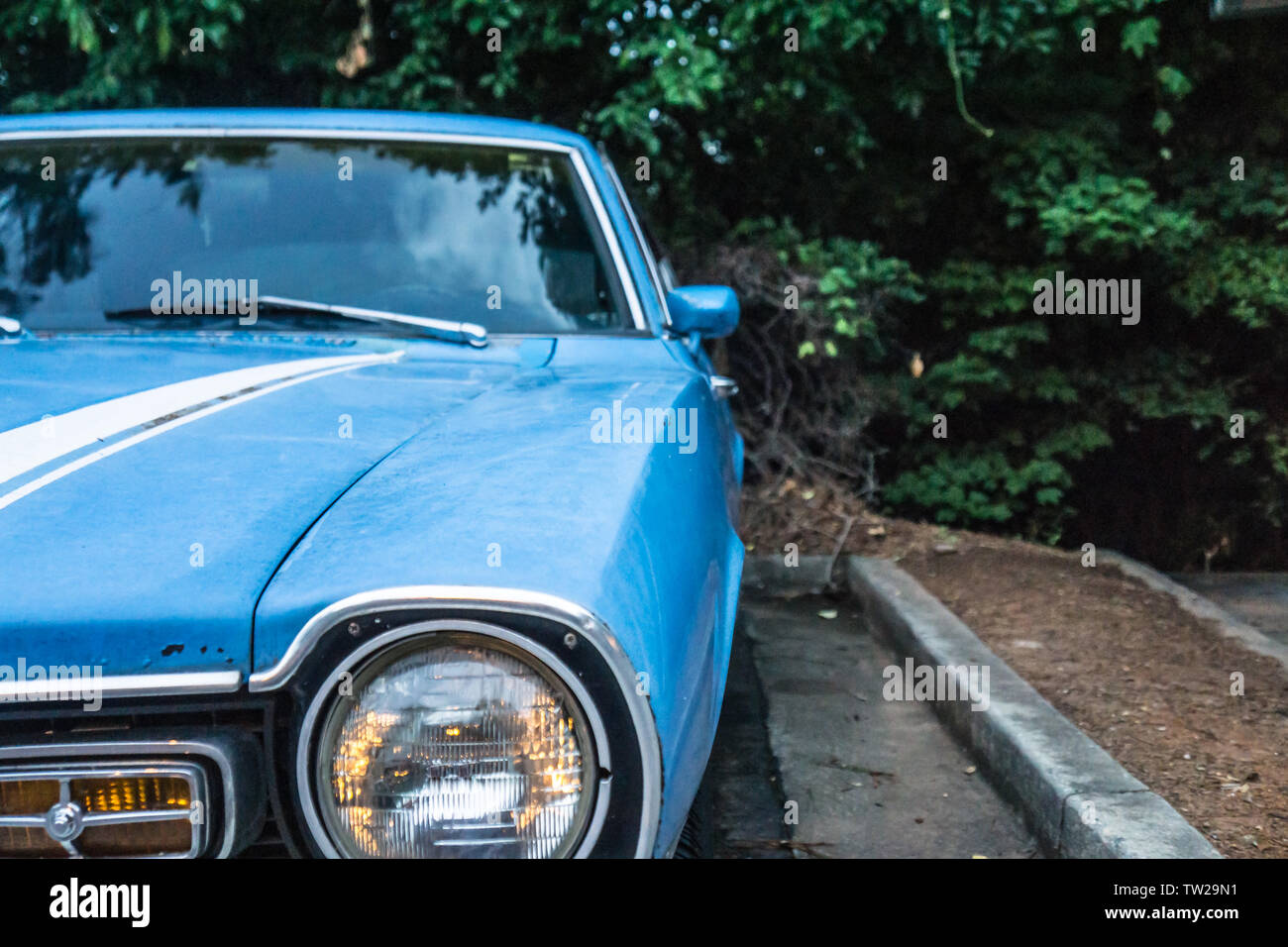 In der Nähe der alten Scheinwerfer's Vintage blaues Auto. Geparkt und umgeben von grünen Bäumen Laub außerhalb. Kein Mensch, aber in der Nähe der Fahrerseite hinten Stockfoto