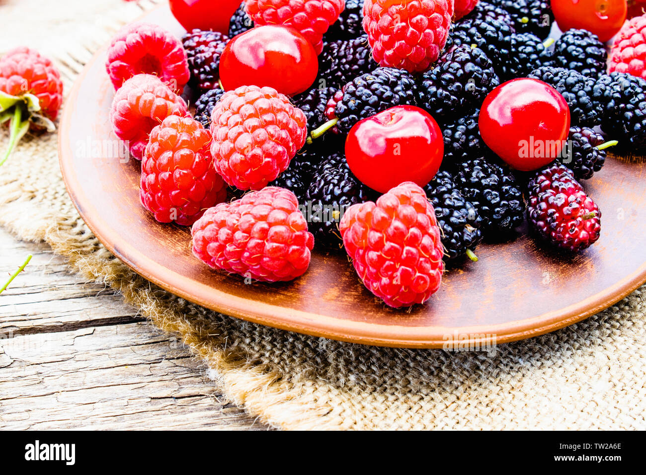 Gemischte Beeren, Kirschen, Himbeeren, Maulbeeren in einer Schüssel auf der Leinwand und Holz- Hintergrund. Close-up Stockfoto