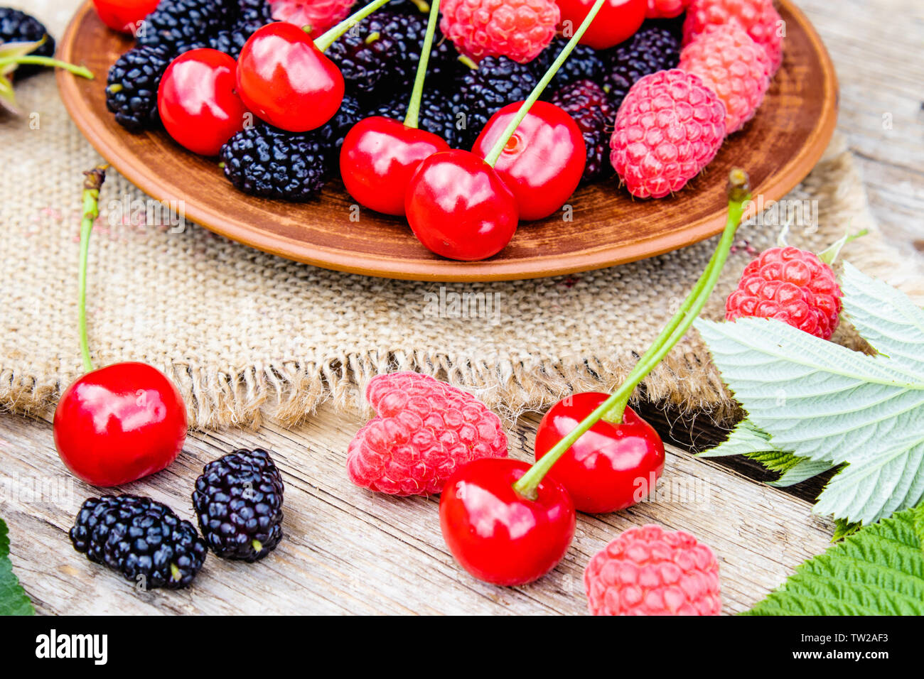 Gemischte Beeren, Kirschen, Himbeeren, Maulbeeren in einer Schüssel auf der Leinwand und Holz- Hintergrund. Close-up Stockfoto
