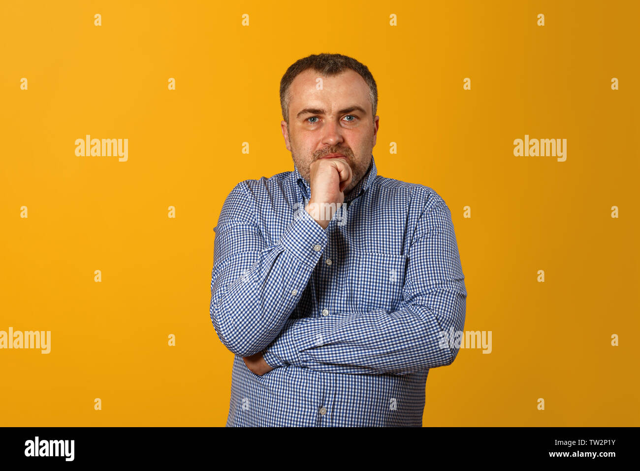Nachdenklicher Mann mit der Hand am Kinn und Kamera. Gelber Hintergrund. Closeup Portrait. Stockfoto