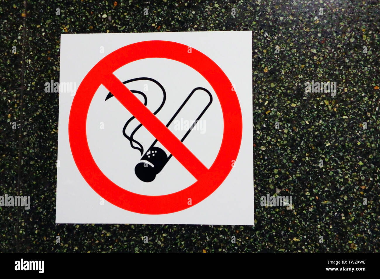 Weißer Aufkleber mit roten Kreis mit Kreuz auf dem Rauchen Zigarette gegen schwarze Marmor Bürowand, kein Rauchen Ikone auf dunklem Stein, in der Nähe Stockfoto