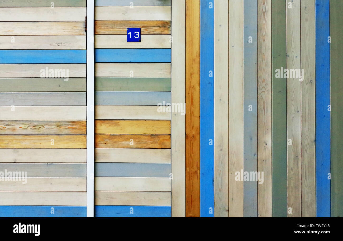 Haus Wand und Tür aus Holz bunt teilweise verblasst Bretter vertikal und horizontal angeordnet. Kleine blaue Schild mit der Nummer 13 auf Stockfoto