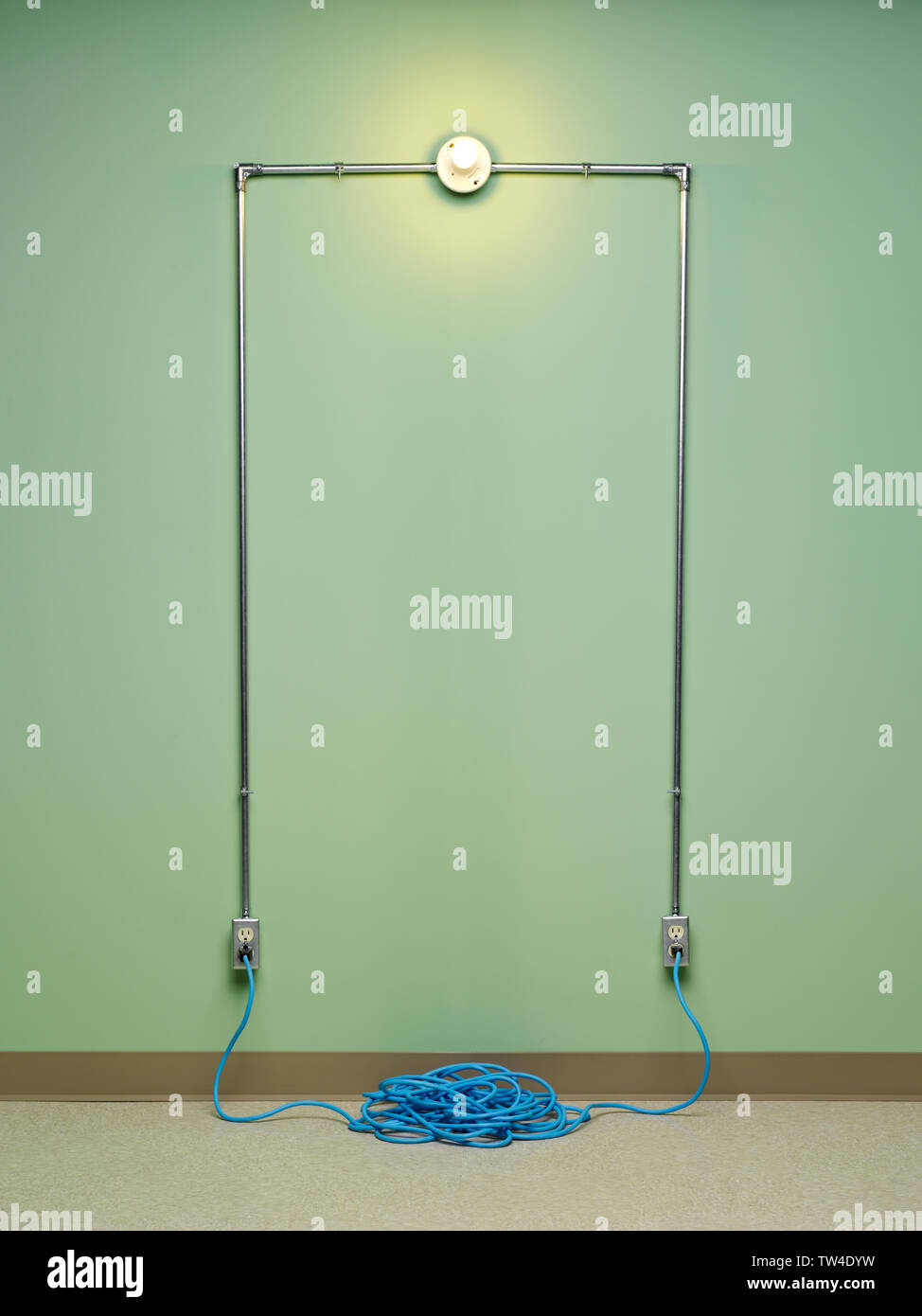 Inkompetent und gefährliche elektrische Schaltung mit blau Spiralkabel Verlängerungskabel angeschlossenen in zwei AC-Steckdosen mit Glühlampen Licht auf grüne Wand Stockfoto