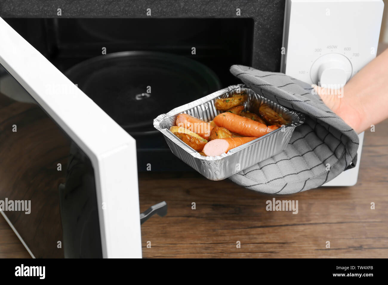 Frau unter Folie Backform mit Kartoffeln und Würstchen aus der Mikrowelle  in der Küche Stockfotografie - Alamy