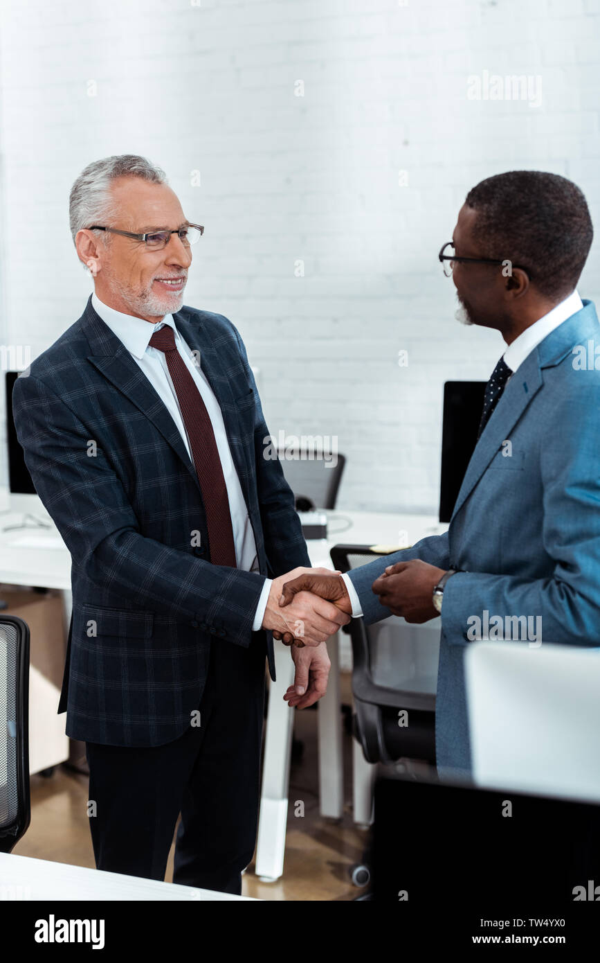 Selektiver Fokus der fröhlichen Geschäftsmann in Gläser Händeschütteln mit afrikanischen amerikanischen Partner Stockfoto