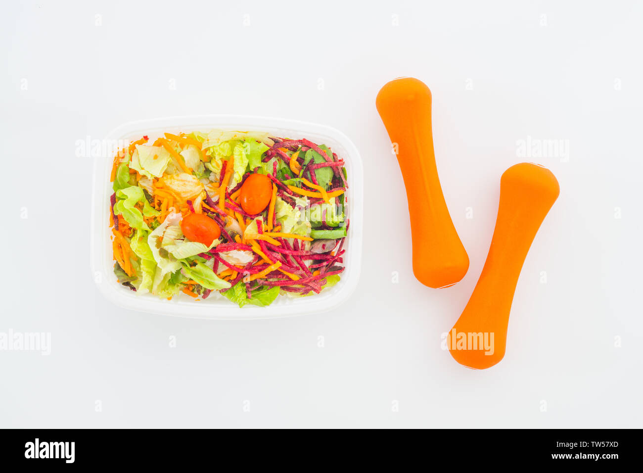 Frisches Gemüse Salat in der Brotdose mit orange Kurzhanteln excercise Ausrüstung auf Weiß. Aktive, gesunde Lebensstile, Gesundheit Konzept. Flach top vi. Stockfoto