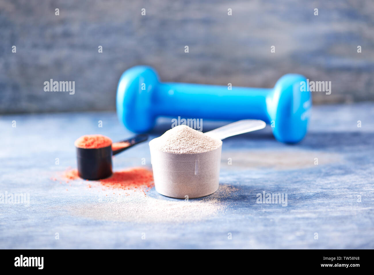 Messlöffel Whey Protein, Creatin Pulver und blau Hantel im Hintergrund Stockfoto
