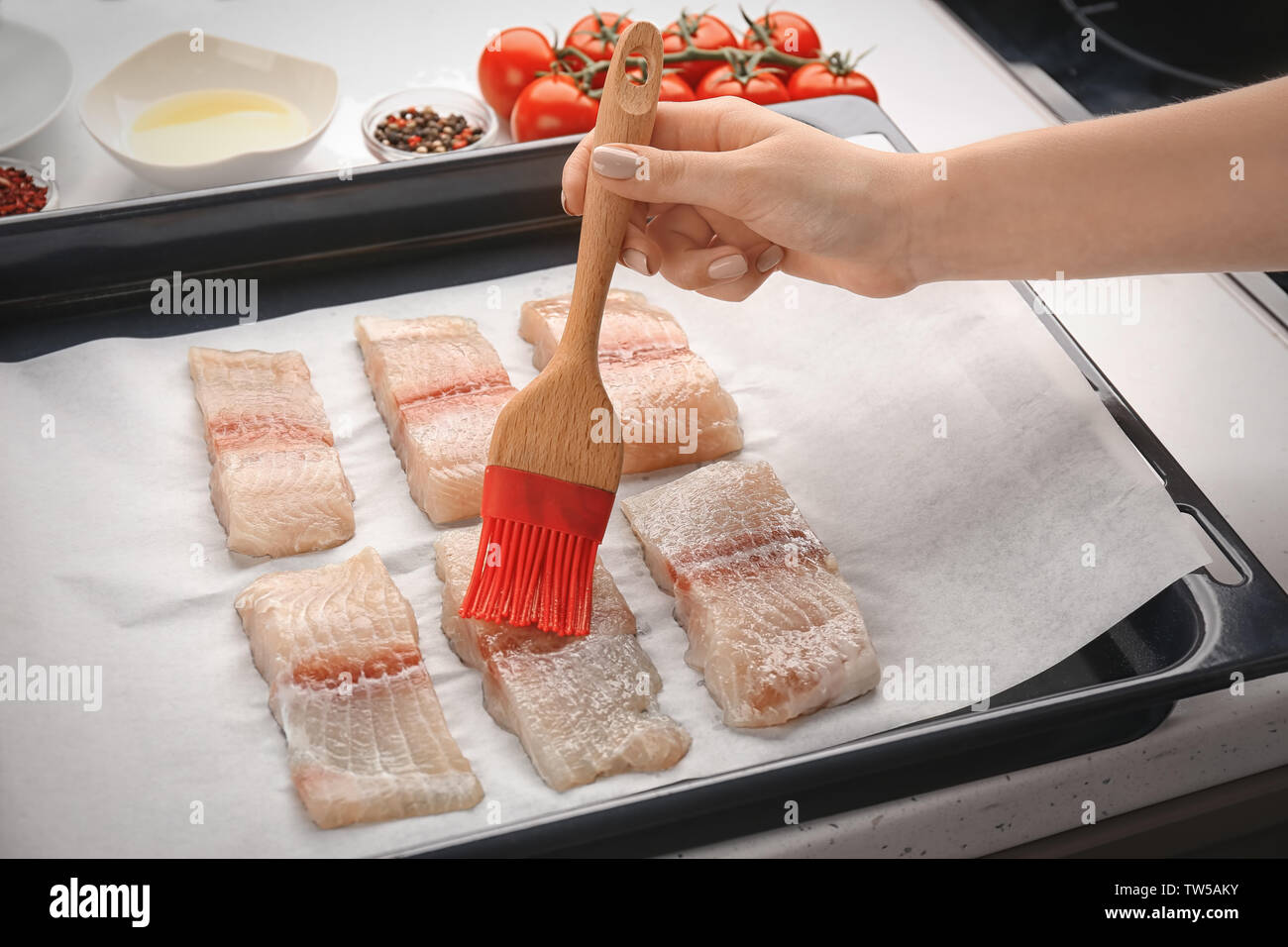 Frau Anwendung Öl auf Fisch Filet Schichten mit Silikon Pinsel in der Küche Stockfoto