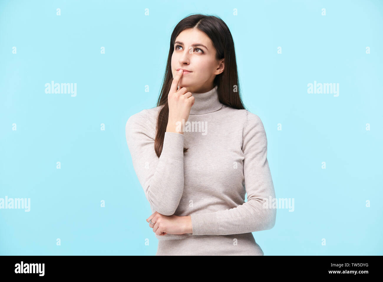 Porträt einer schönen jungen kaukasischen Frau, nachdenken, den Finger auf die Lippen, bis suchen, auf blauem Hintergrund isoliert Stockfoto