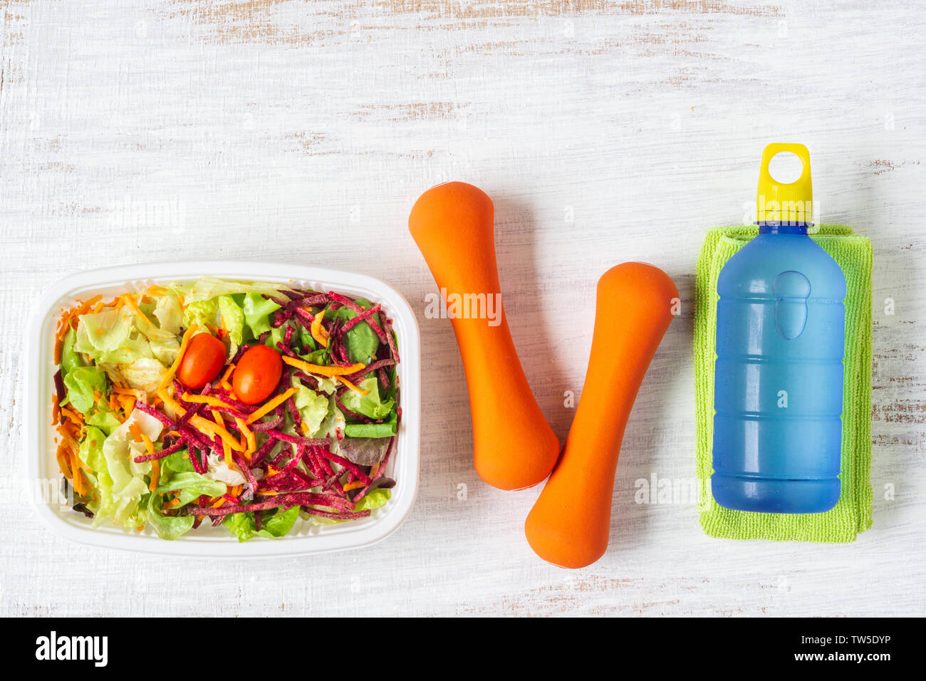 Frisches Gemüse Salat in der Brotdose mit orange Kurzhanteln übung Ausrüstung und Energie Wasser trinken auf Weiß rostig Holz Hintergrund. Aktiv gesund lif Stockfoto