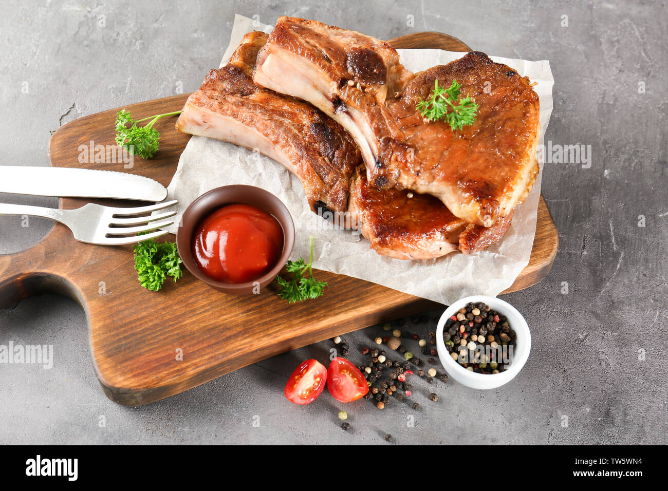 Holzbrett mit köstlichen gegrillten Rippchen und Tomatensauce auf Tisch Stockfoto