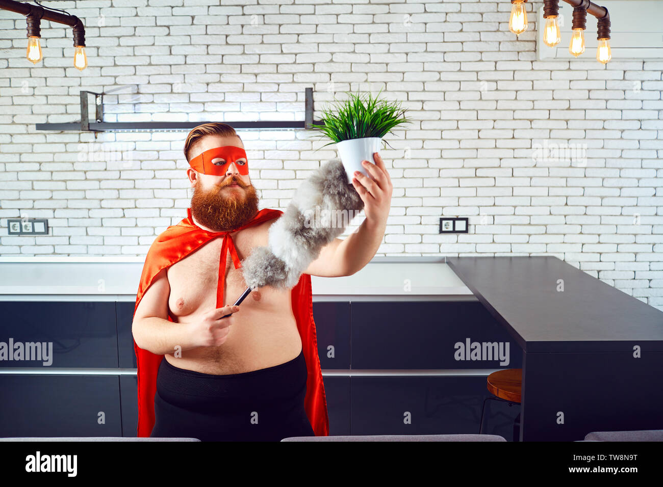 Ein fettes, lustige Mann in einen Superhelden Kostüm ist Reinigung des Hauses. Stockfoto