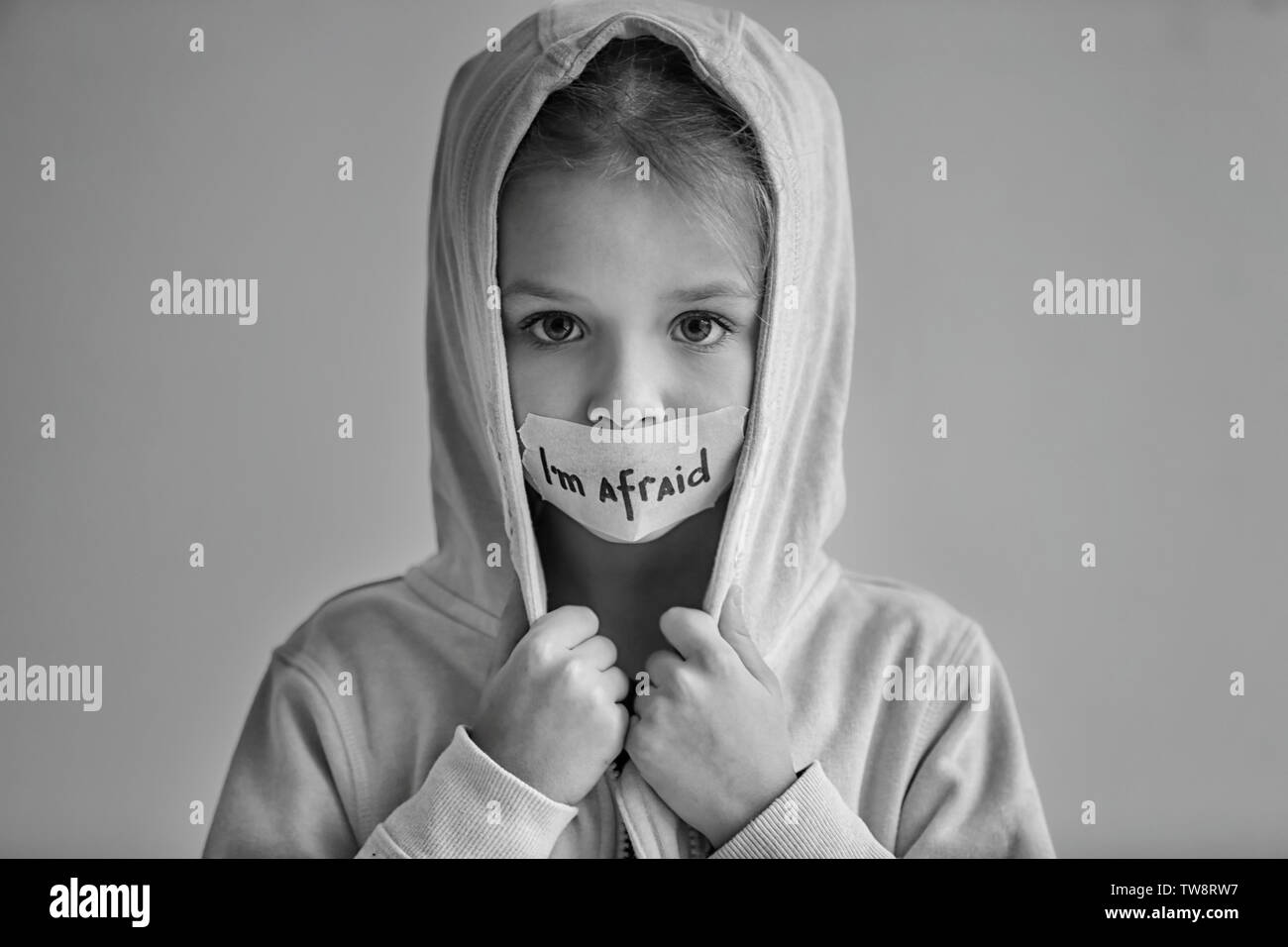 Trauriges kleines Mädchen mit Getapten Mund und die Worte 'Ich bin auf grauem Hintergrund Angst", Schwarzweiß-Effekt Stockfoto