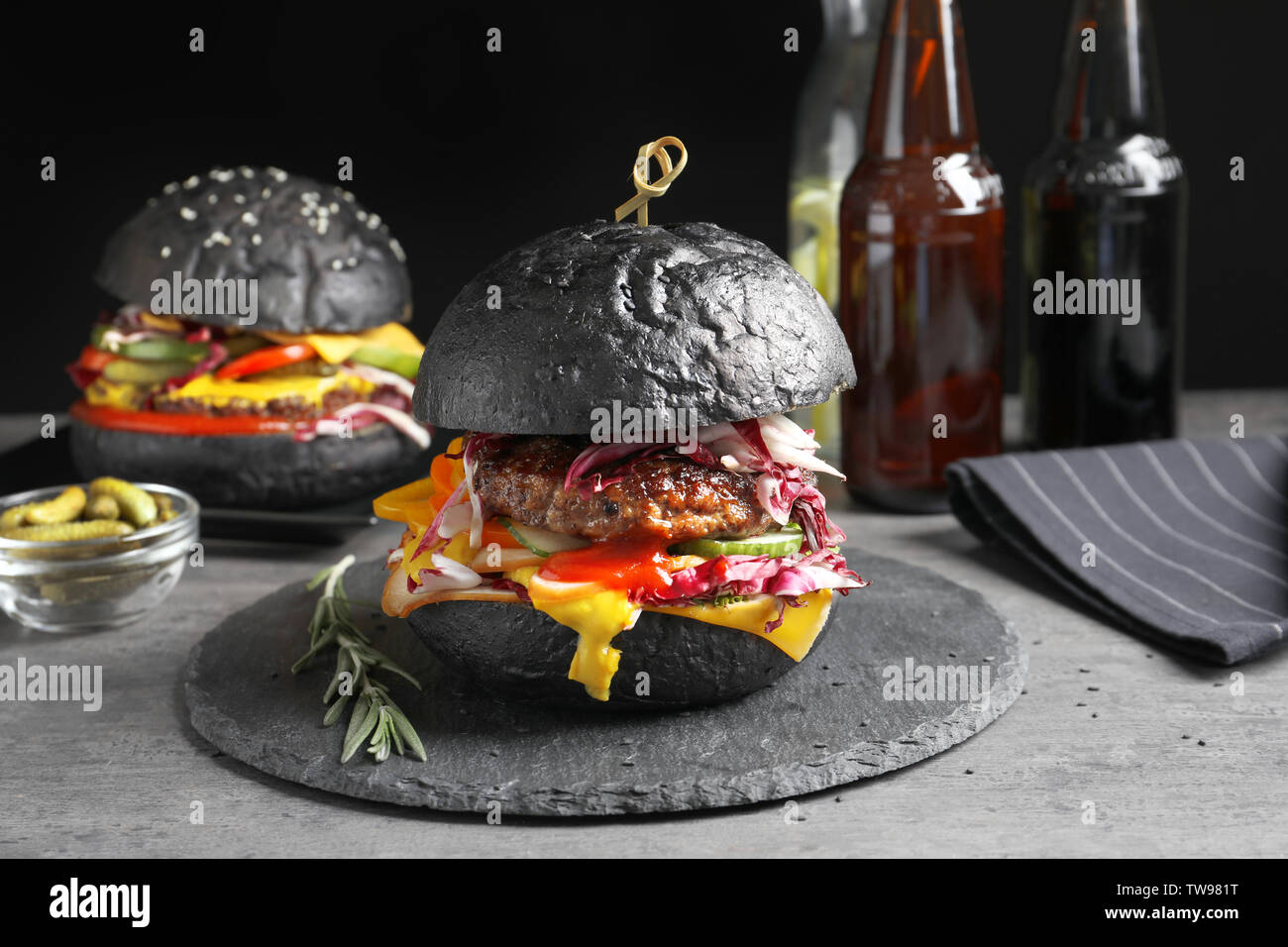 Schiefer Teller mit leckeren schwarzen Burger auf Tisch Stockfotografie
