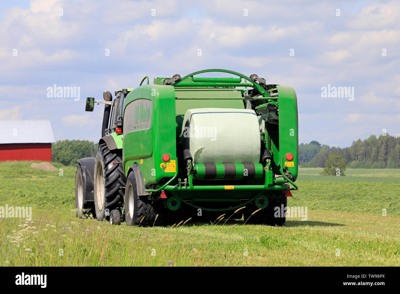 Salo, Finnland. Juni 15, 2019. Deutz-Fahr Schlepper und McHale 3 plus Pressen Pressen von Silage in grün Kunststoff Blatt im Heu Feld an einem sonnigen Tag im Sommer. Stockfoto