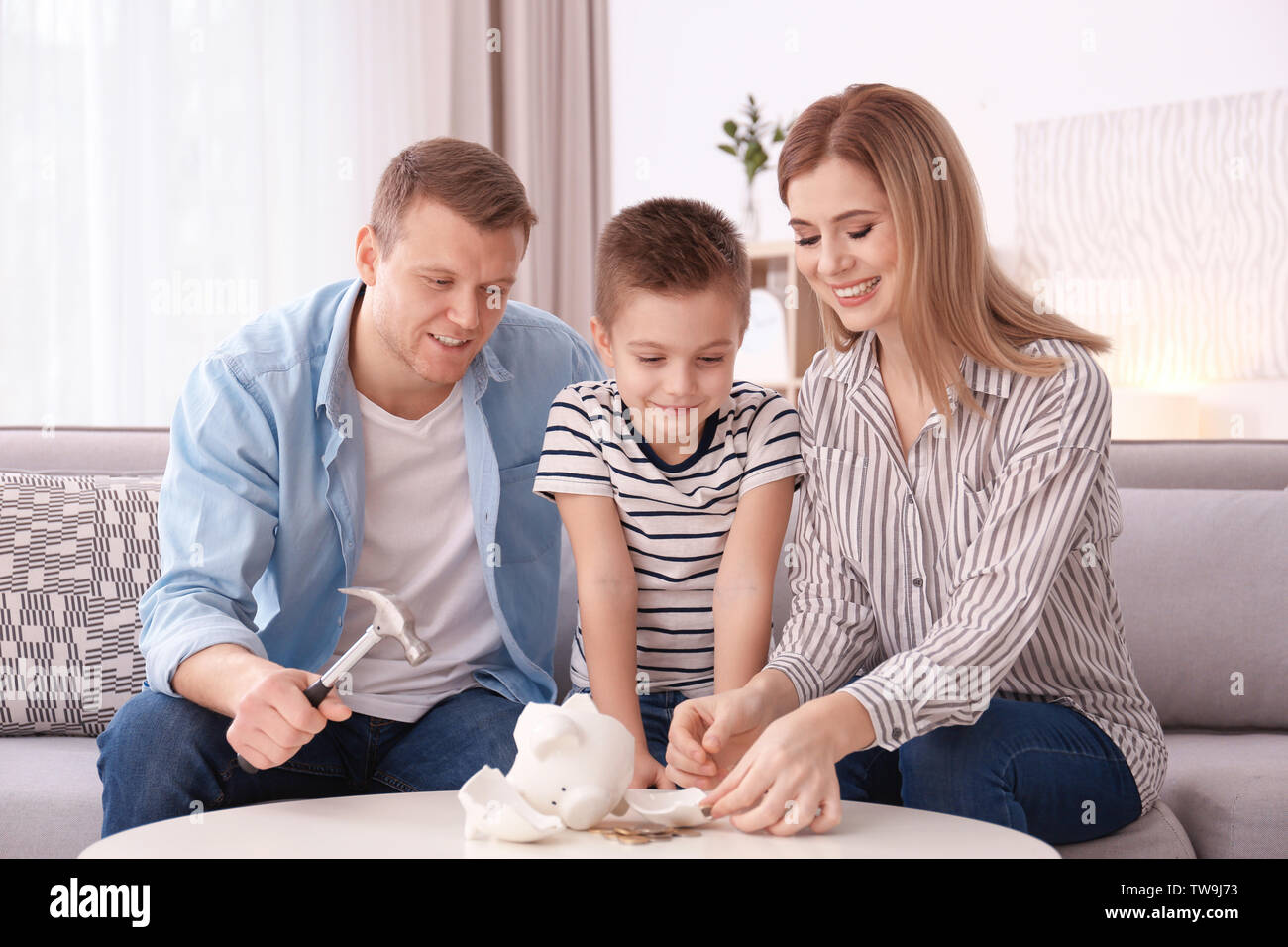 Glückliche Familie brechen Sparschwein mit Hammer zu Hause Stockfoto