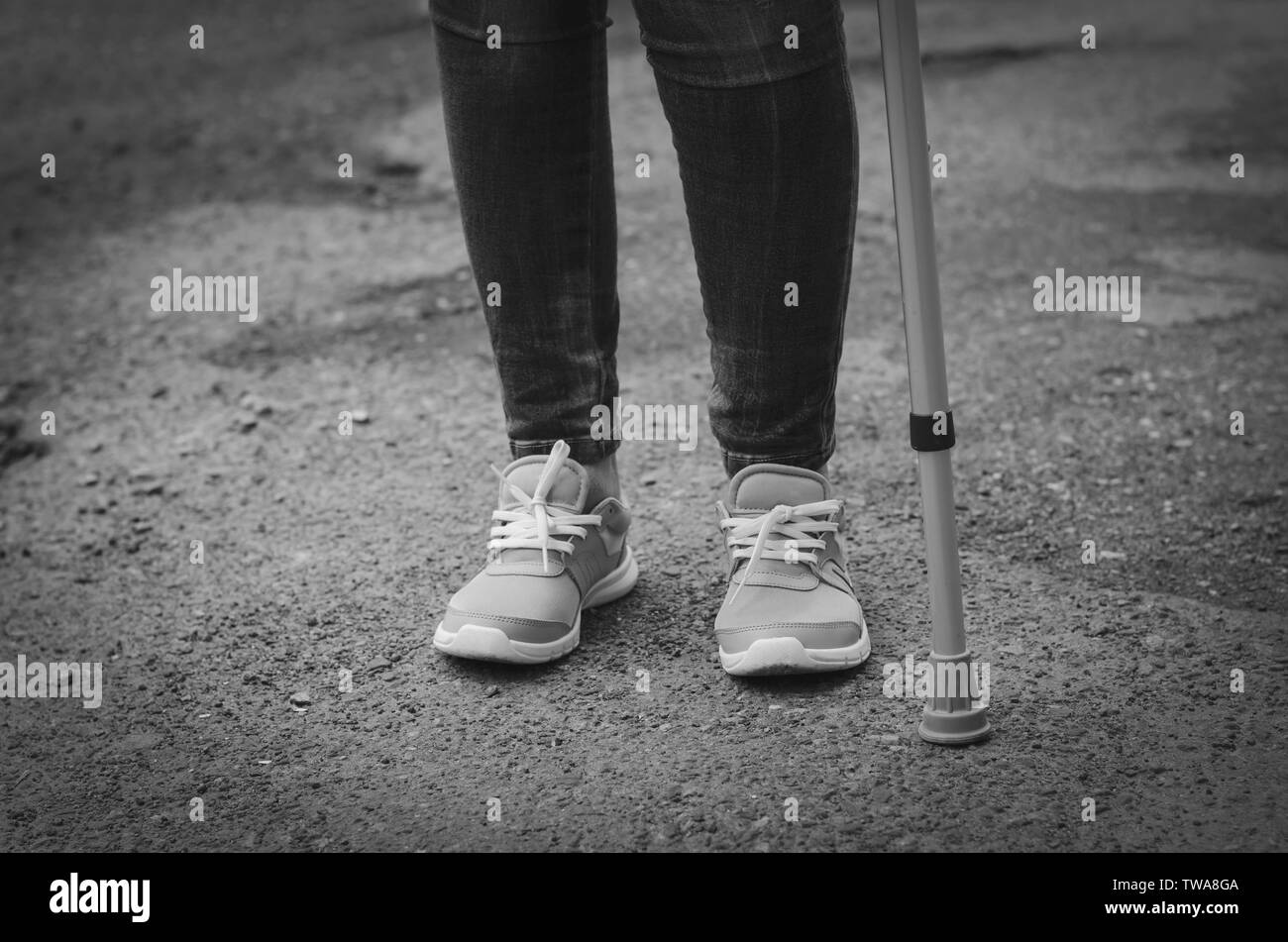 Ältere Frau in Jeans mit Spazierstock im Freien. Rehabilitation und Recovery Konzept. Schwarz und Weiß. Platz kopieren Stockfoto