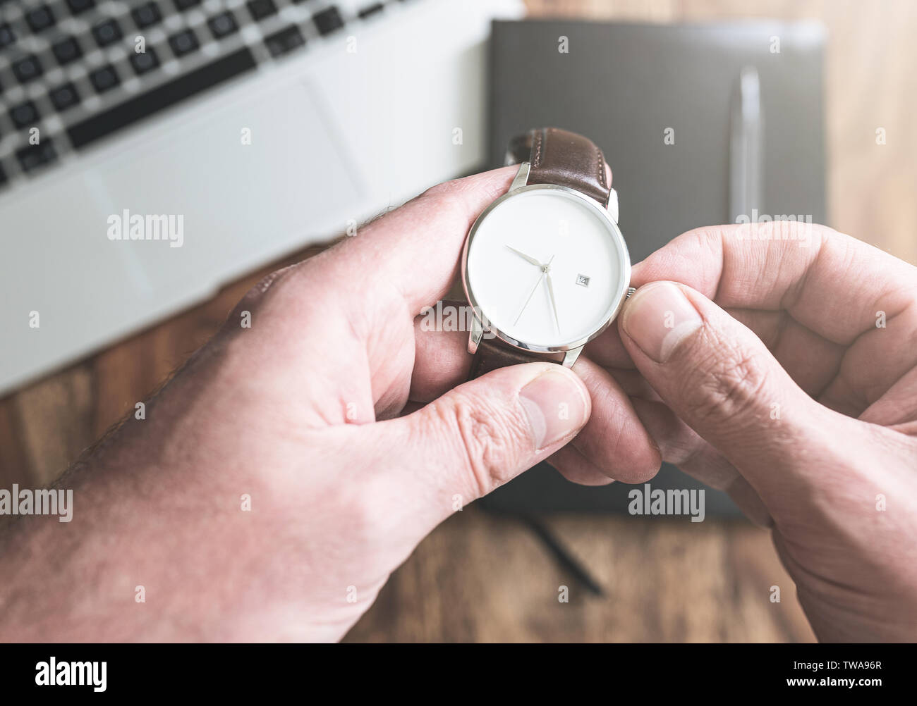Der Mensch seine Armbanduhr gegen Laptop und persönlichen Organizer auf hölzernen Schreibtisch einstellen Stockfoto