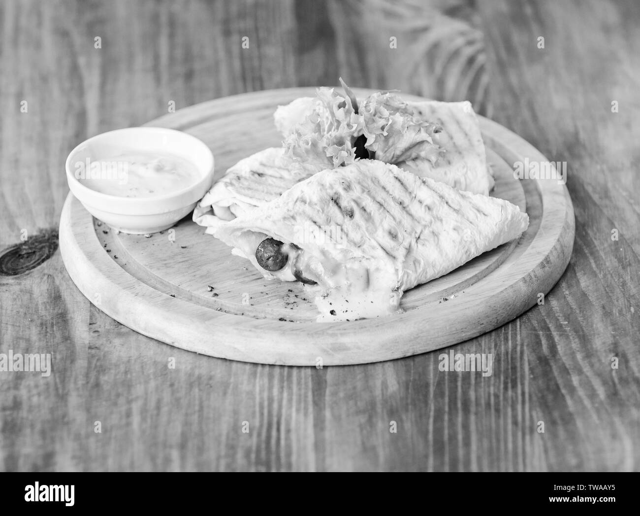 Essen im Restaurant traditionelle Küche. Burrito tortilla serviert Holzbrett. Das Essen im Restaurant Konzept. Lavash burrito gefüllt Fleisch Wurst und Käse sauce Salat serviert. Fleisch umhüllt mit lavash Burrito. Stockfoto
