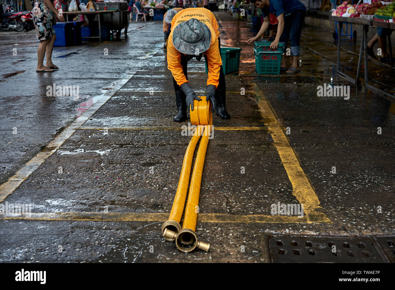 Straßenreinigung rollt den Schlauch nach der Reinigung zu einem Thailand markt Veranstaltungsort. Stockfoto