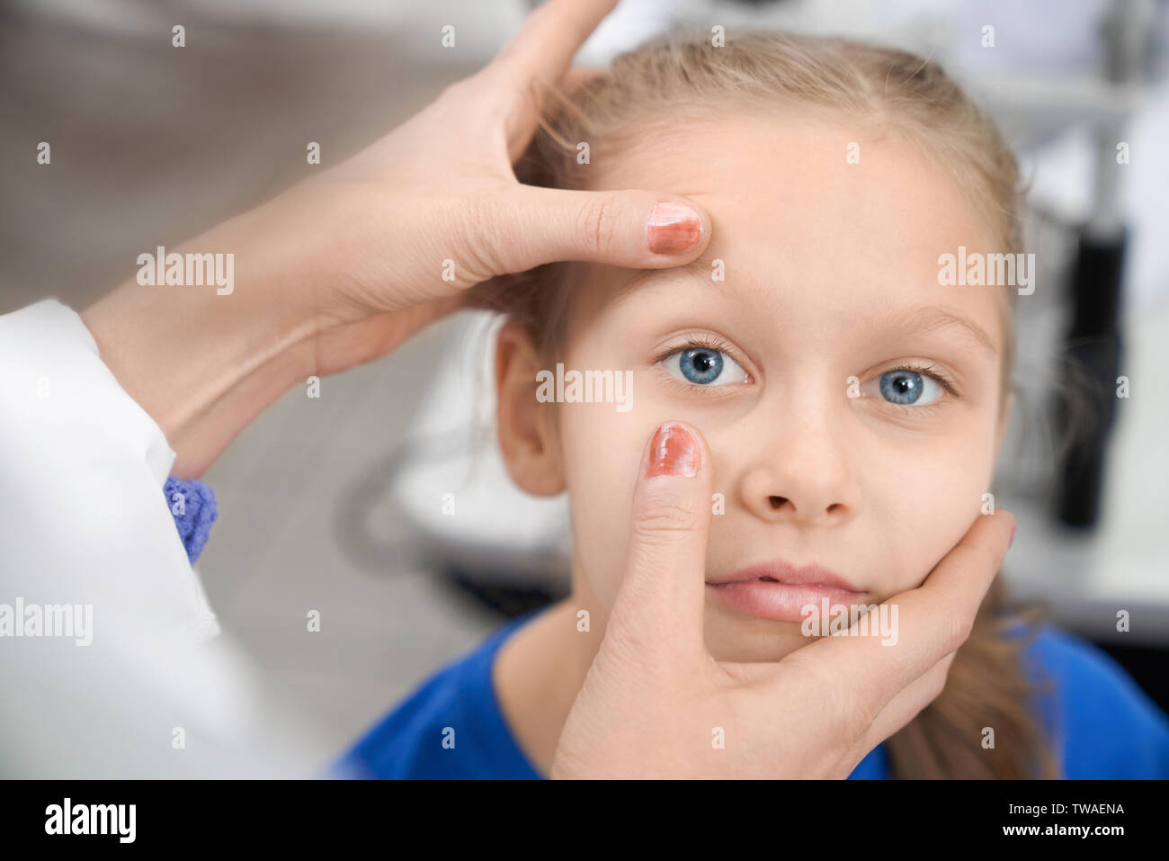 Nahaufnahme der Mädchen an der Kamera suchen, während die weiblichen Augenarzt prüfen Vision in der Klinik. Kind mit blauen Augen sitzen in optischen Speichern, während Arzt auf Augenhöhe Schüler suchen. Konzept der medizinischen Untersuchung. Stockfoto