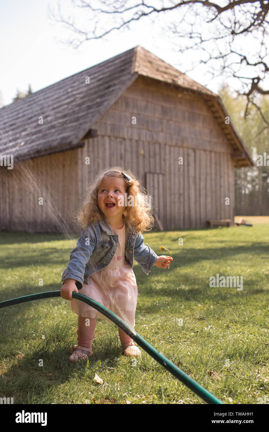 Schönes, glückliches Mädchen mit lockigem Haar, in Sommer Spaß, schreien in der Aufregung, Spielen im Freien mit Wasser besprüht aus Gartenschlauch Stockfoto