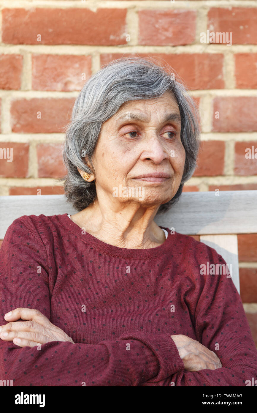 Ältere Asiatische indische Frau alleine sitzen. Gesund und schlank aussehen, kann auch darzustellen, Einsamkeit oder Depressionen im Alter. Stockfoto